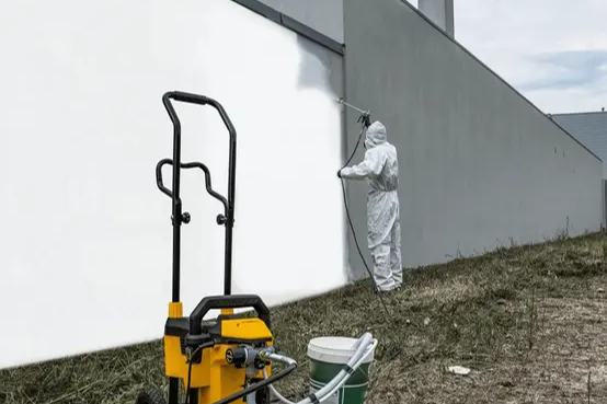 Peintre en combinaison projetant de la peinture blanche sur une façade